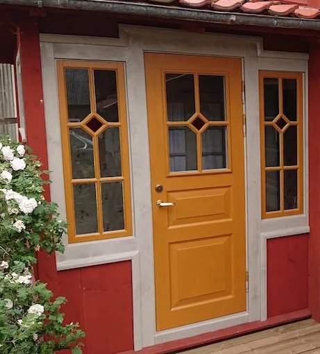 Två gula ytterdörrar med glasfönster och gråa karmar på en husvägg med röda paneler och vita lister.