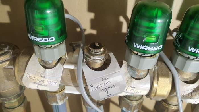 Närbild av en golvvärmefördelare med etiketten "Badrum" och avlägsnat ställdon.
