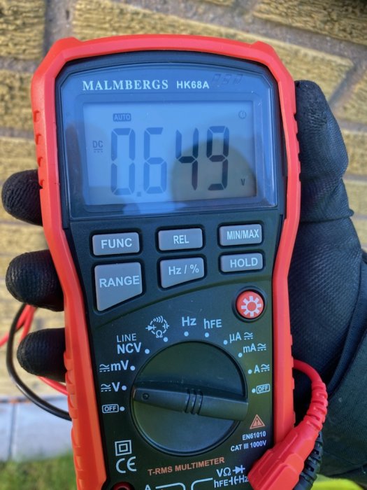 Multimeter visar 0.649 V DC spänning, hand i svart handske håller i instrumentet.