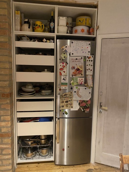 Vardagskök med öppna skåplådor fyllda med köksredskap och en kyl med magneter och lappar.
