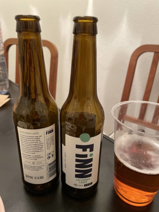 Två tömda flaskor Finn California Lager bredvid ett halvfullt ölglas på ett bord.