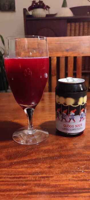 Ett glas fyllt med röd glögg bredvid en burk märkt "GLÖGG SOUR" på ett träbord.