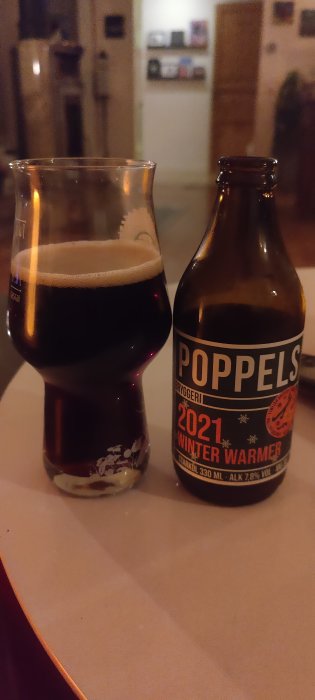 Flaska av Poppels Winter Warmer öl bredvid ett glas fyllt med mörkt öl på ett bord.