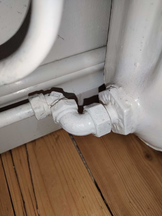 Vitt rörledningsarbete vid fotlisten, med synliga tecken på reparation eller försegling.