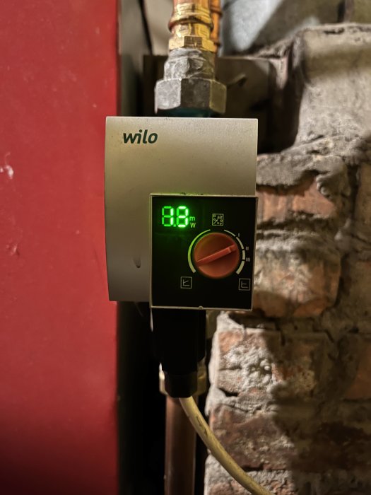 Wilo cirkulationspumpens display visar 88°C, monterad på rörledning med stenbakgrund.