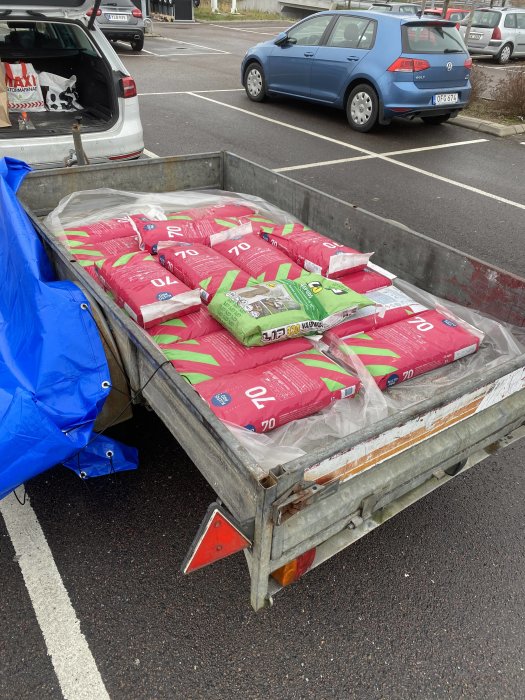 Släpvagn full med säckar av byggmaterial parkerad på en parkeringsplats.