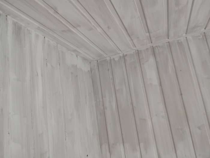 Vitmålad träpanel på vägg och tak med synliga penseldrag och ojämn täckning.