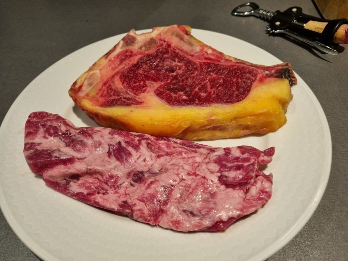 Enkelbiff och pluma iberico råa på en vit tallrik bredvid en vinöppnare.