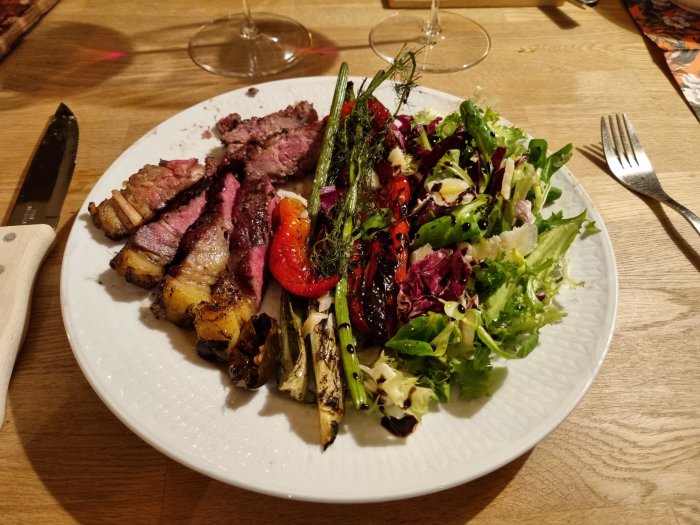 Tallrik med grillade biffar och pluma iberico, sallad, grillade grönsaker på ett träbord.