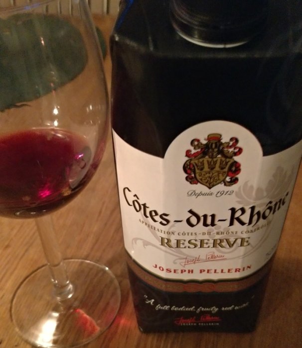 Glas med rödvintill hälften fyllt och en flaska Côtes du Rhône Réserve vin.