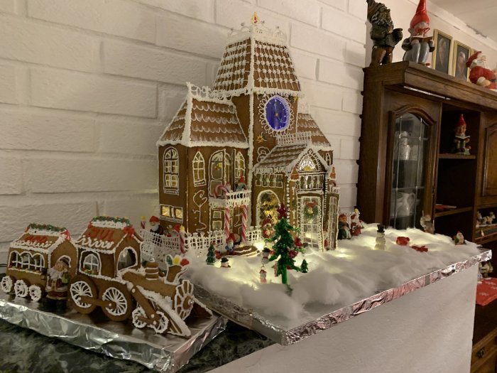 Handgjort pepparkakshus med dekorationer och en pepparkakståg på ett juldekorerat bord.