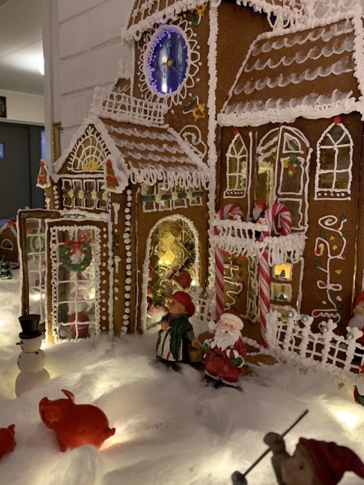Detaljerad pepparkakshus med juldekorationer, belysning och figurer som föreställer julgranar och tomten.