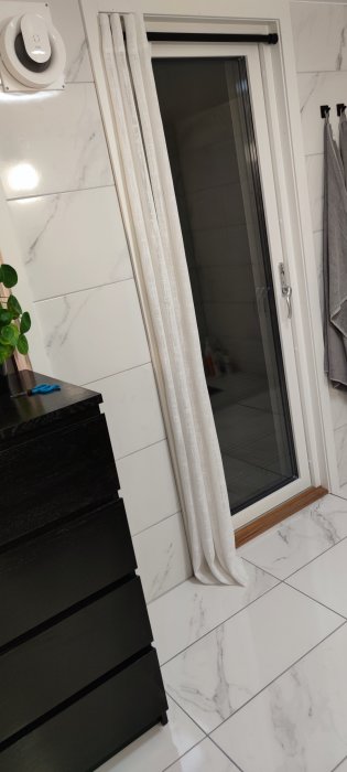 Nyligen renoverat badrum med marmormönstrade kakelväggar, vita golvplattor och svart badrumsmöbel.
