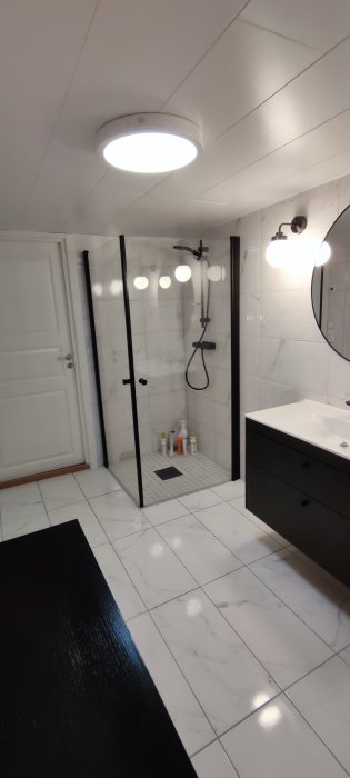 Nyligen renoverat badrum med marmorliknande kakel, glasduschkabin och modern handfatsskåp.