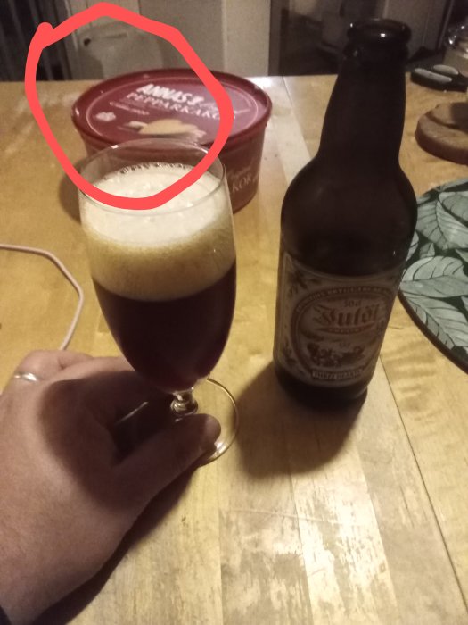 Hand håller ett ölglas, en ölflaska och pepparkaksburk på bord.