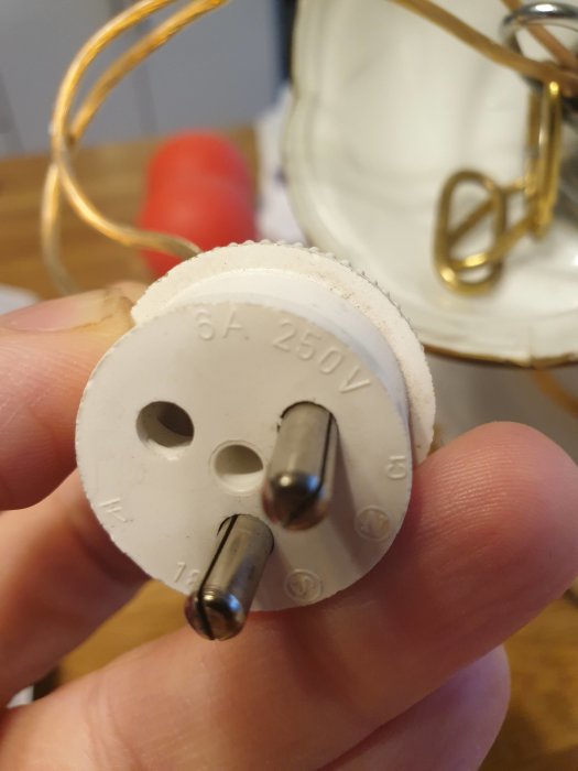 Hand håller en vit elektrisk propp märkt med "6A 250V" avsedd för byte för anpassning till takuttag.