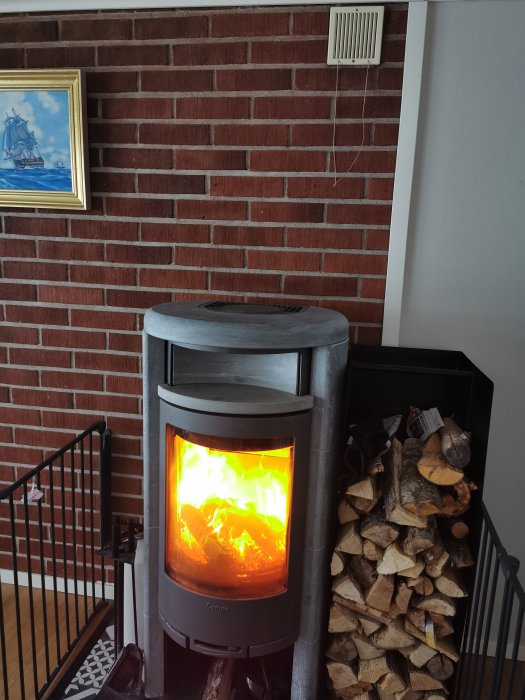 Eldad kamin med brinnande ved och en frånluftsventil ovanför på en tegelvägg.