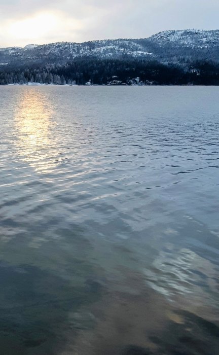 Solnedgång speglar sig i en stilla sjö med snötäckta berg i bakgrunden.