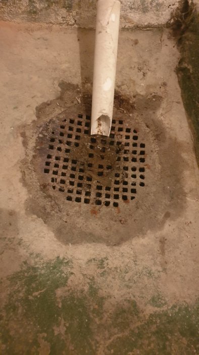 Gammal gjutjärnsbrunn i en källare, med synliga rör och slitage, nära en vägg.