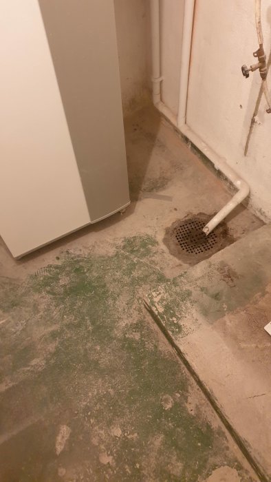 Gammal gjutjärnsbrunn intill betongvägg och rör i ett källarrum under renovering.