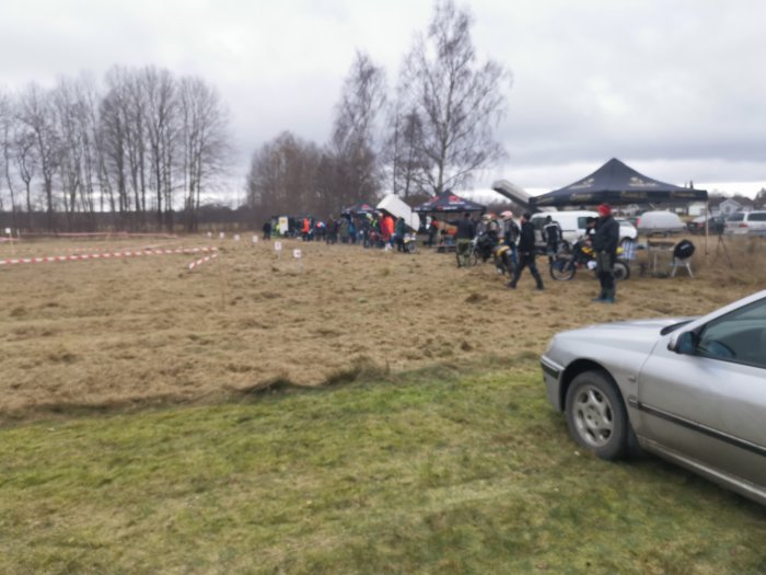 Människor och mopeder vid årliga stubbracet på ett fält med tält och racingbana avspärrad med band.