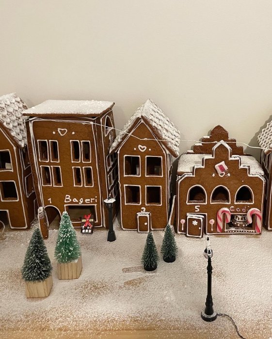 Pepparkakshus formade som byggnader och träd med "snö", och en gatlykta på ett bord.