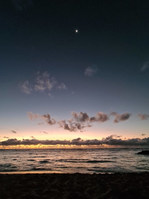 Solnedgång över havet med moln på himlen och en skymt av månen.