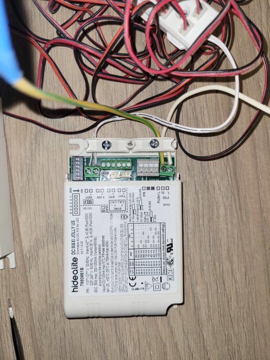 En transformator för spotlights med anslutna kablar och installationsinstruktioner på en träyta.