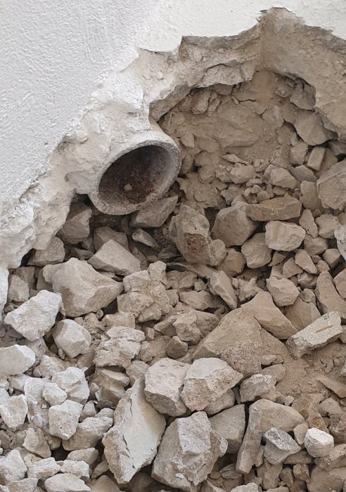 Uppbruten betonggolv som avslöjar ett gammalt avloppsrör som leder till en av tre brunnar i en källare.