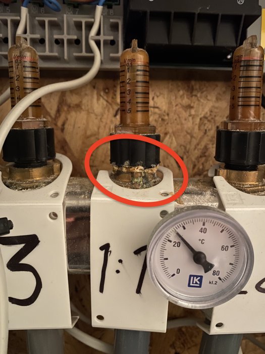 Värmesystem med korroderade rörkopplingar markerade med en cirkel, flödesmätare och en termometer visande cirka 20 grader Celsius.