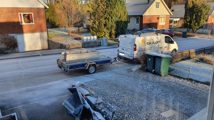 Byggmaterial lastat på släp och en skåpbil från Nordic Solar parkerad utanför ett hus.