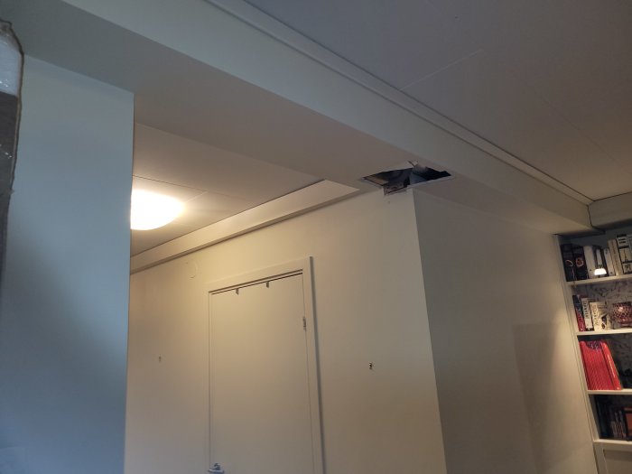 Delvis skadad balk i hörnet av en öppning i taket, med synlig struktur ovanför en dörr.