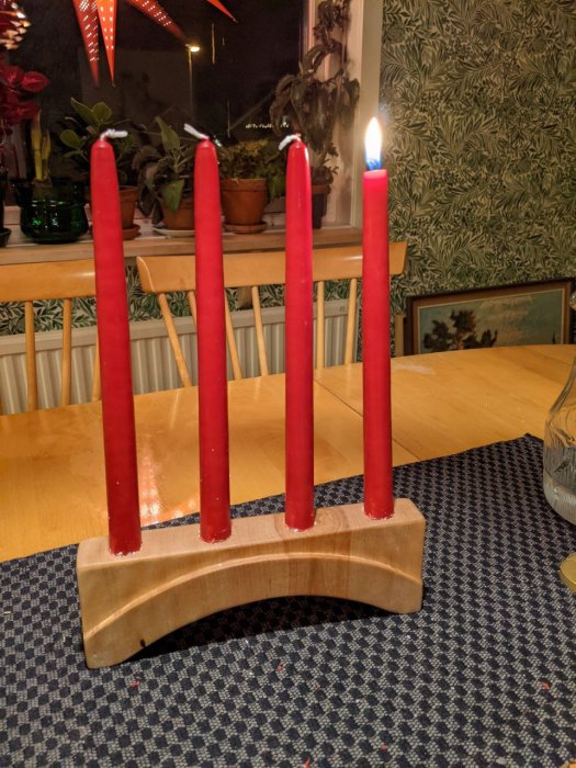 Hemsnickrad träljusstake med fyra röda adventsljus, ett tänt, på ett köksbord.