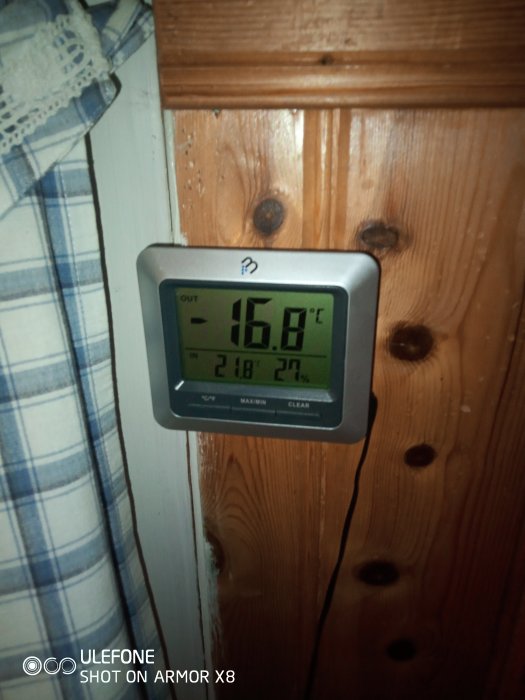 Digital termometer som visar -16,8°C ute och 2,8°C inne på en trädvägg.