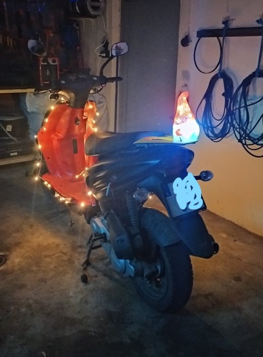 Motorcykel i garage dekorerad med ljusslinga, intill en lysande julgran.