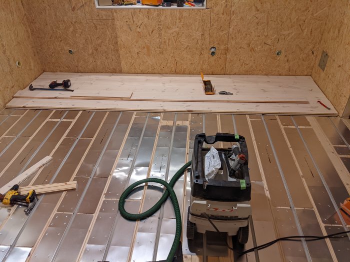 Delvis lagt trägolv med verktyg och golvbrädor på undergolv i ett byggprojekt.