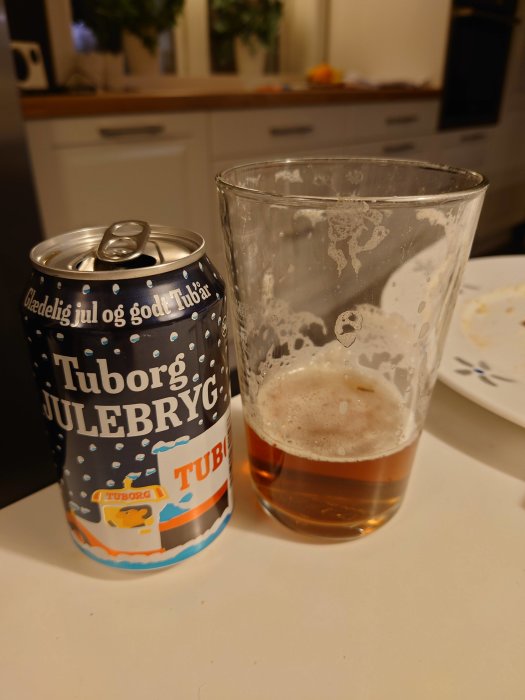 Delvis drucket glas med julöl och öppnad Tuborg Julebryg-burk på köksbord.