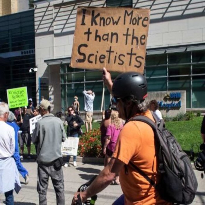 Person håller en skylt med texten "I Know More than the Scietists" under en demonstration.