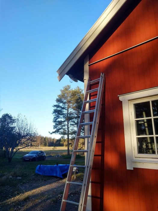 Nyligen installerad utebelysning på ett rött hus i skymningen med en stege lutad mot fasaden.