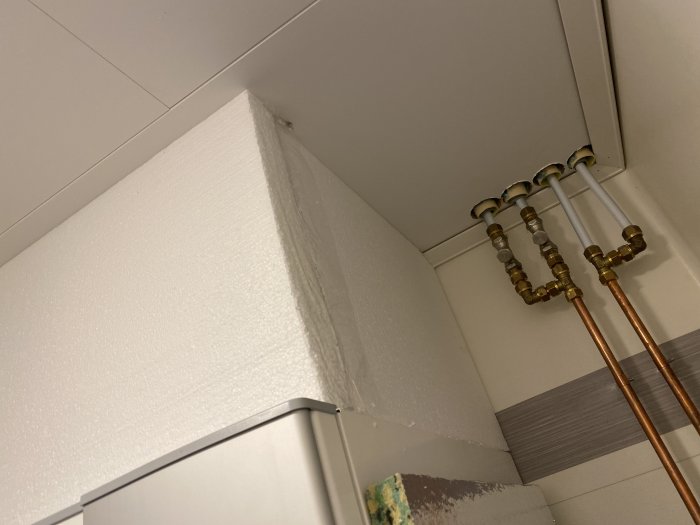 Ett hörn i ett badrum med synliga vattenrör och kakel under installation.