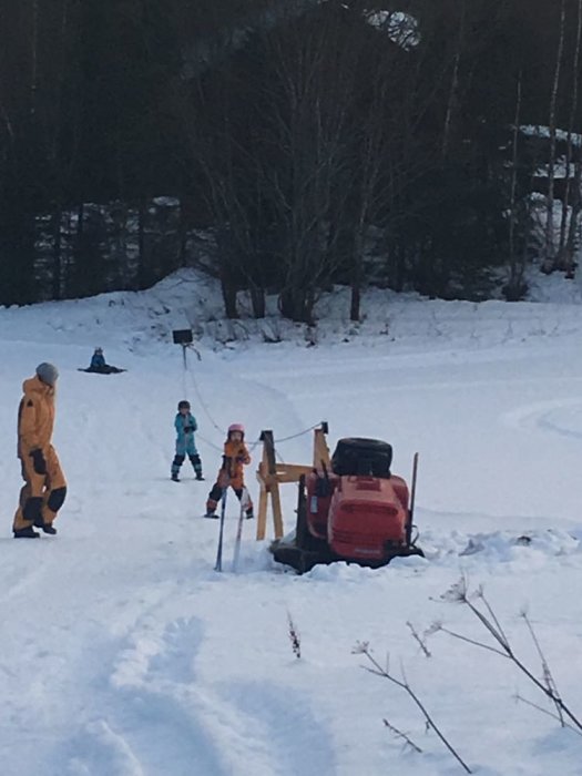 Egenbyggd släplift med gräsklippare och barn som åker pulka i en snötäckt backe.