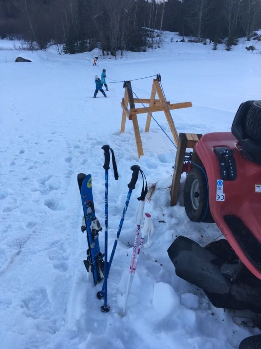 Hemmagjord skidlift med trädgårdstraktor och enkel träkonstruktion, skidor i förgrunden, barn åker i bakgrunden.