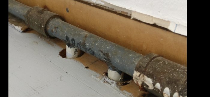 Gamla radiatorrör synliga vid plåtsockel, risk för läckage vid rörskarvar.