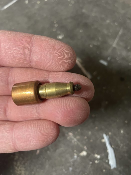 Hand håller en liten metallföremål som liknar ammunition men kan vara ett verktyg.