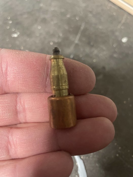 En hand håller ett litet metallföremål som liknar ammunition, eventuellt ett verktyg.