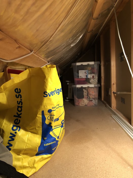 En vind med snedtak och isolering, IKEA-kassar och lådor för förvaring, oljefläckar på golvet.