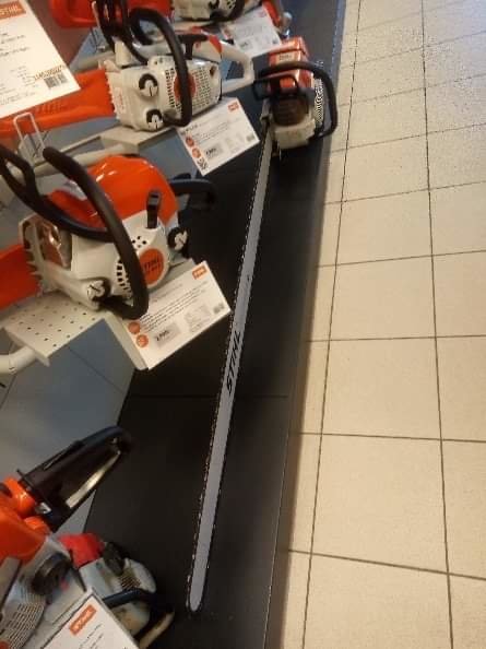 Lång svärdkedjesåg på display i butik med andra motorsågar i bakgrunden.