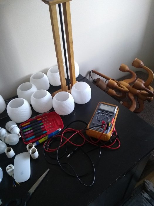 Multimeter med sladdar på ett bord tillsammans med lampdelar och verktyg under lampprojekt.