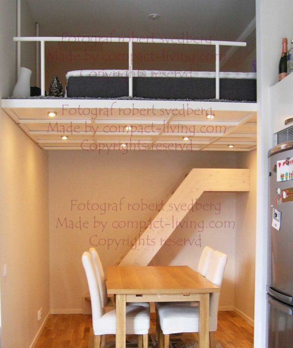 Ett minimalistiskt loft monterat i taket över ett matbord, med synliga stödstolpar och en trästege.