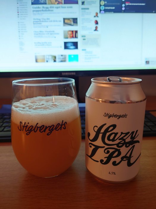 Ett glas fyllt med hazy IPA från Stigbergets framför dator med forum på skärmen, och en burk av samma öl bredvid.